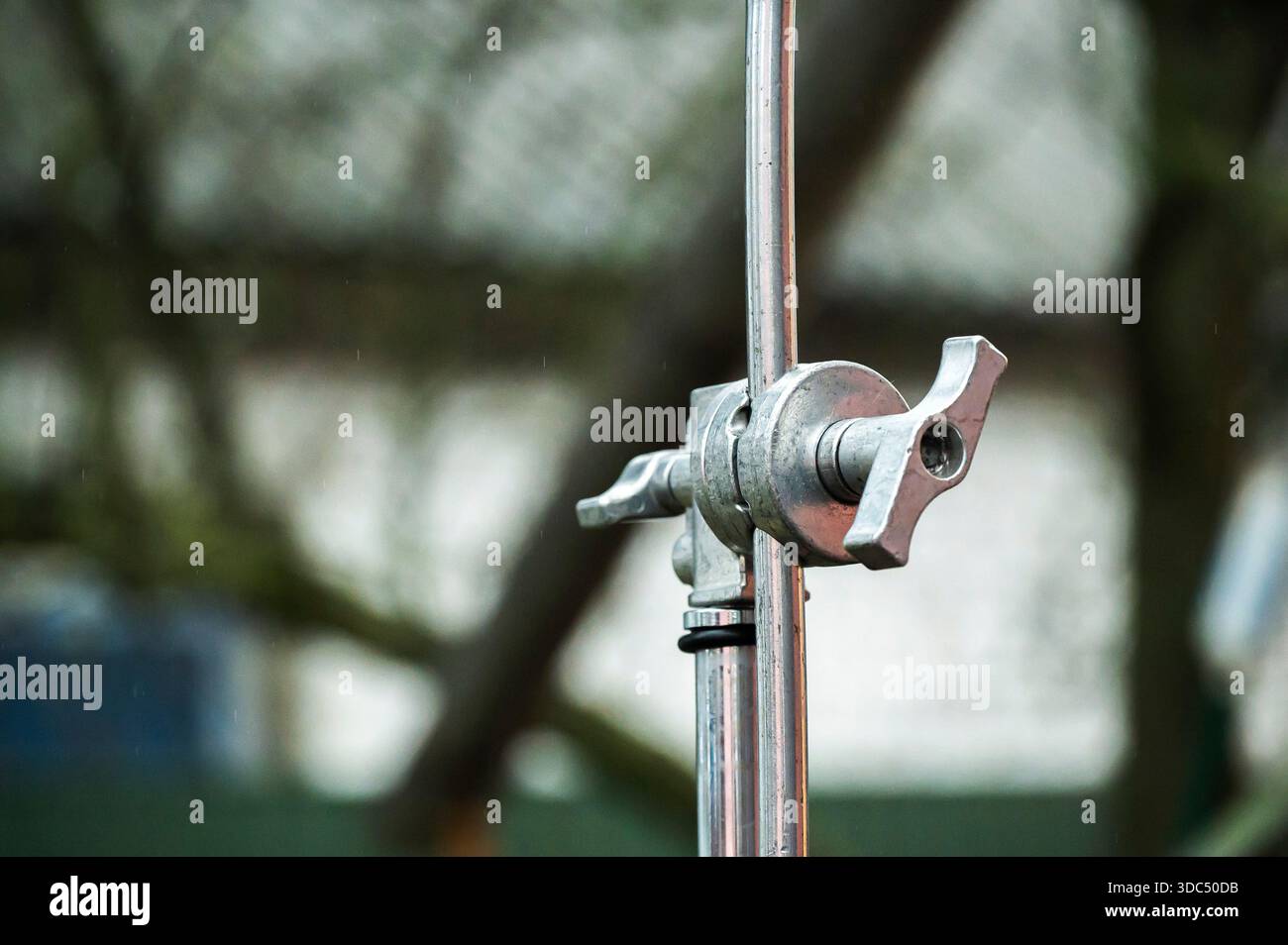 Testa con impugnatura in metallo che controlla un supporto a C per fotografia, parte dell'apparecchiatura essenziale di un set di pellicole commerciali, con un morbido sfondo sfocato che suggerisce bac Foto Stock