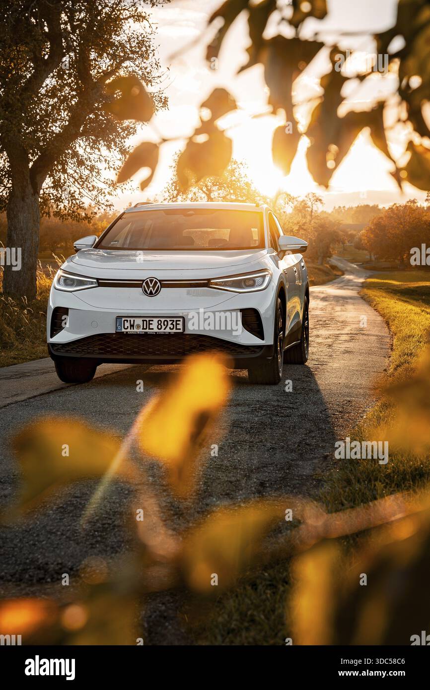 Auto bianca su una strada di campagna al tramonto circondata da foglie, auto elettrica VW ID4, Deer Carsharing, Calw, Germania Foto Stock