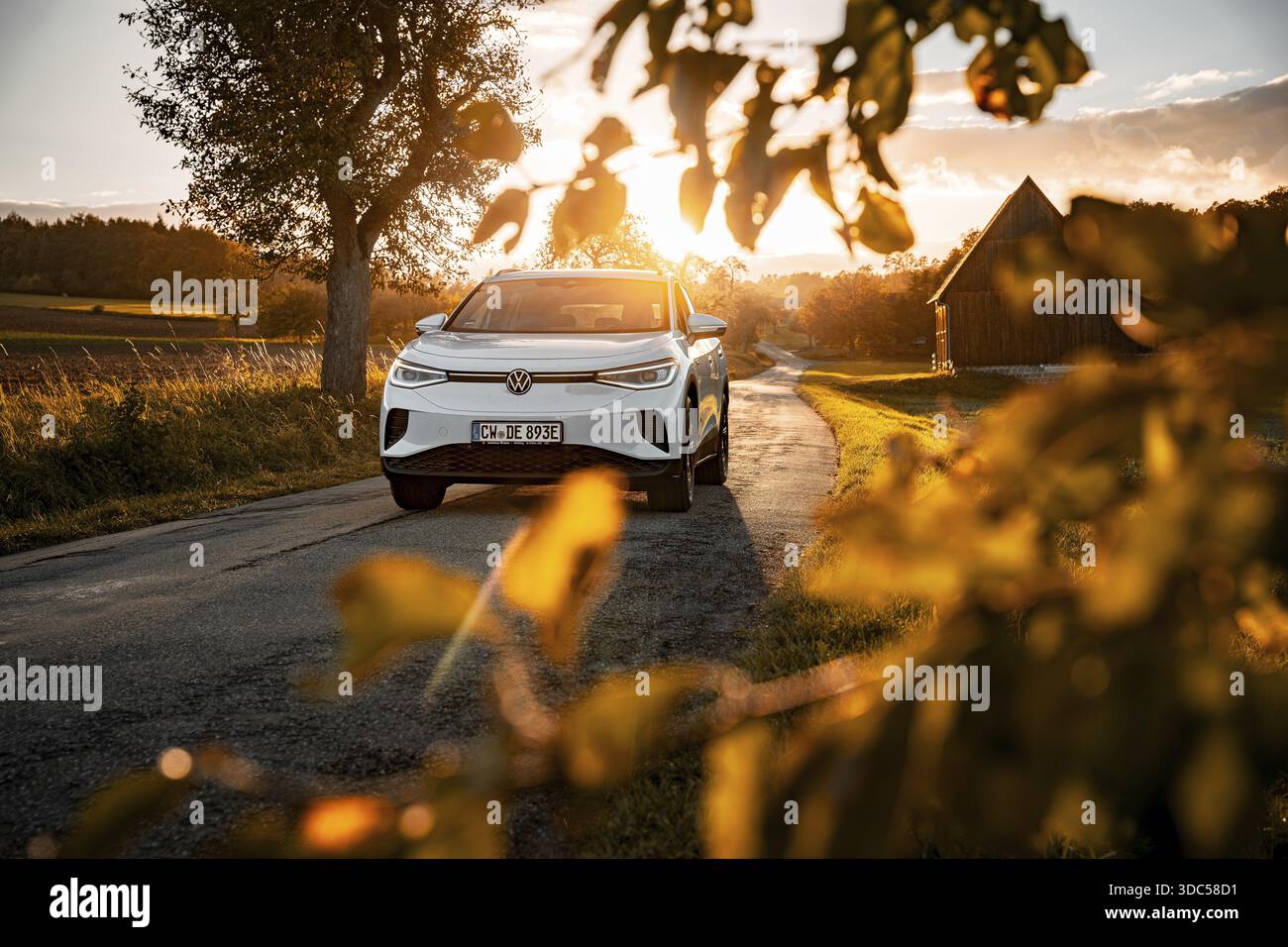 Auto bianca al tramonto sulla strada con una fattoria sullo sfondo, auto elettrica VW ID4, Deer Carsharing, Calw, Germania Foto Stock