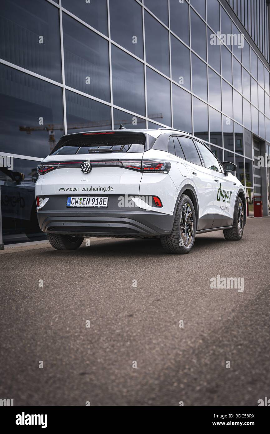 Auto bianca davanti alla facciata in vetro su strada asfaltata, auto elettrica VW ID4, Deer Carsharing, Calw, Germania Foto Stock