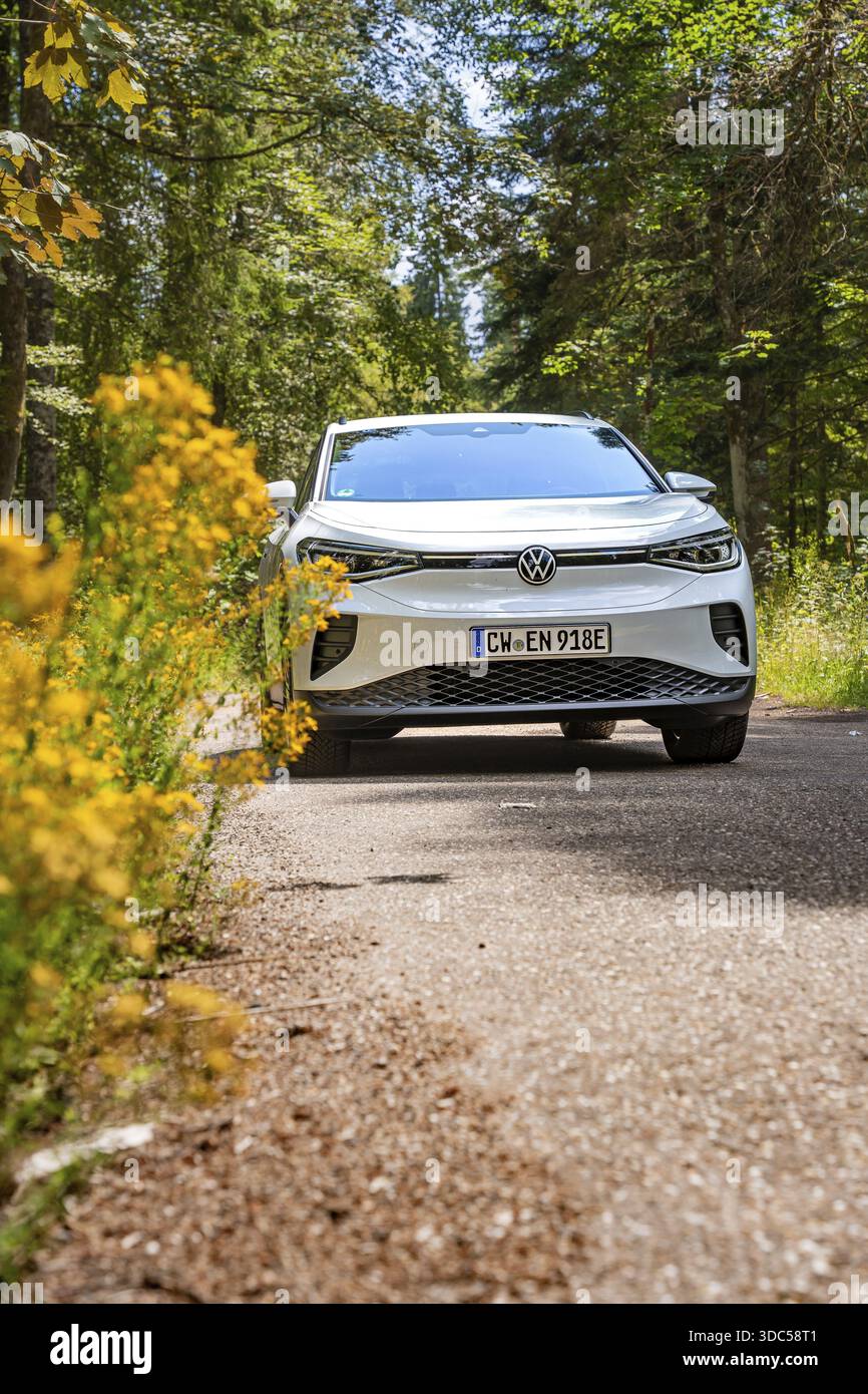 Volkswagen bianca su una strada forestale con fiori gialli in primo piano, auto elettrica VW ID4, Deer Carsharing, Calw, Germania Foto Stock