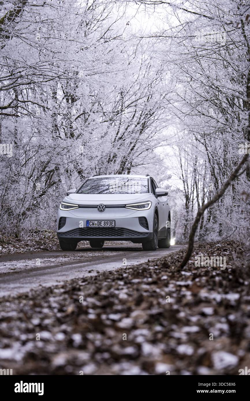 Auto bianca su strada innevata in una foresta innevata, auto elettrica VW ID4, condivisione di auto con cervi, Calw, Germania Foto Stock
