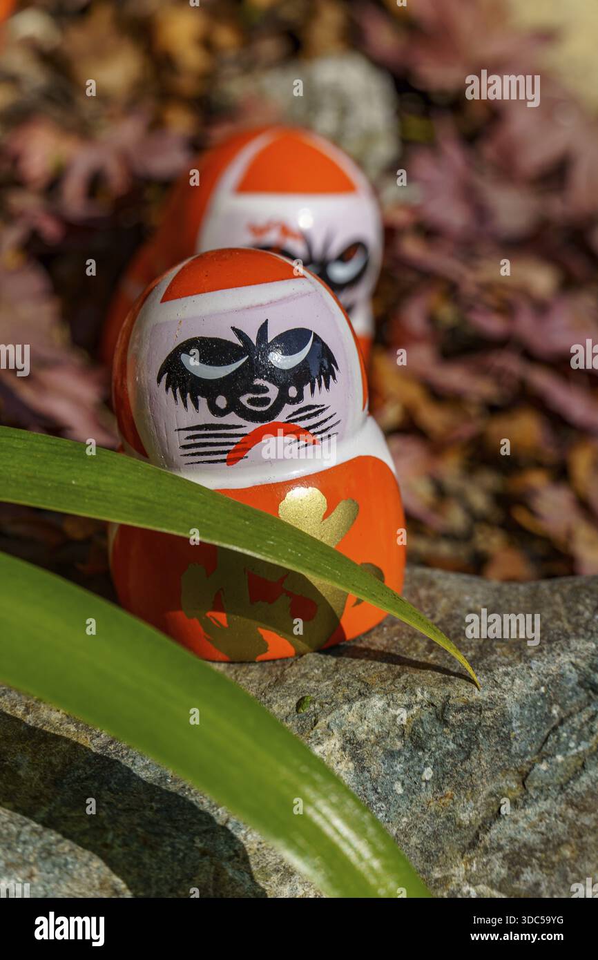 Primo piano di bambole Daruma con dettagli circondati da foglie e pietre, Osaka, Giappone Foto Stock