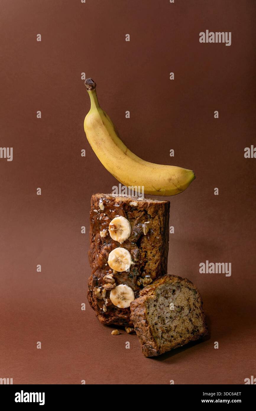 Natura morta moderna con pane alla banana fatto in casa. Pagnotto con noci, caramello condito con banana fresca su fondo marrone. Banana di levitazione abo Foto Stock