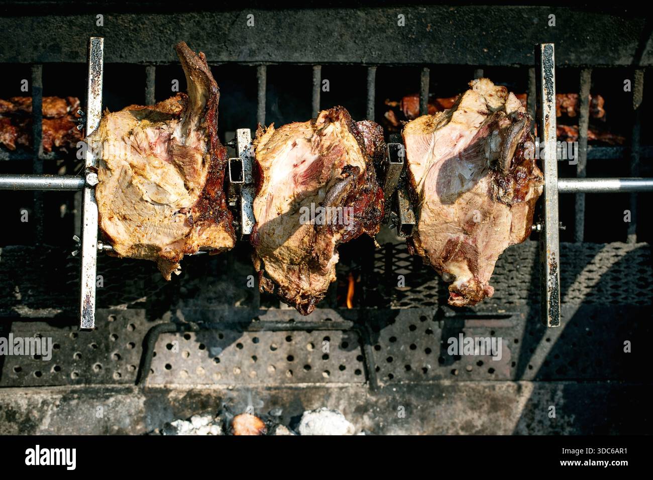 Festival del cibo di strada in Europa. Cibo tradizionale europeo. Tre prosciutti di maiale arrostiti su uno spiedo sopra i carboni caldi al chiosco di cibo all'aperto. Foto Stock