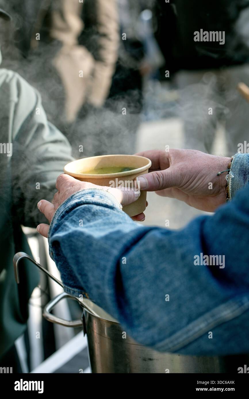 Festival europeo del cibo di strada. Il cliente riceve la mano del fornitore di zuppe calde del recipiente usa e getta. Brodo tradizionale fatto in casa servito all'aperto in un'atmosfera da mercato st Foto Stock