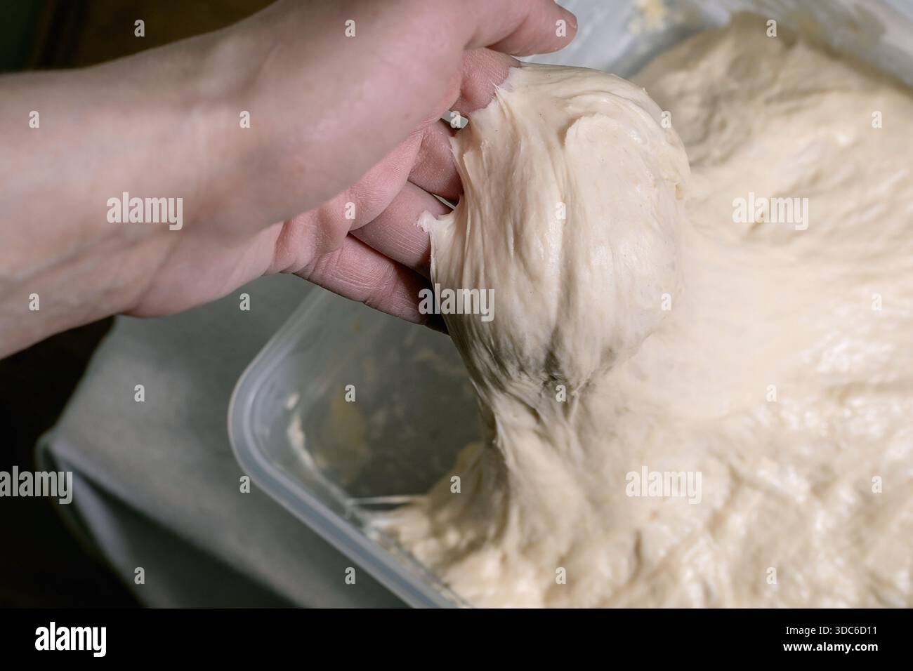 Primo piano di una donna che impasta a mano l'impasto di lievito in un contenitore di plastica. Processo di preparazione del pane fatto in casa che allunga l'impasto elastico per il pane. Foto Stock