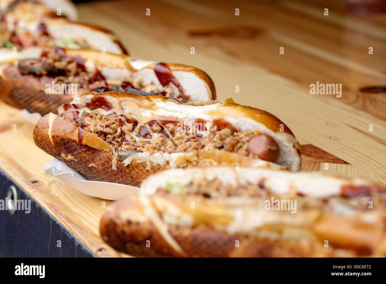 Deliziosi hot dog da buongustai con salsa di carne al formaggio fuso e cipolle servite su panini freschi. Cibo di strada perfetto per festival o cene informali. Foto Stock