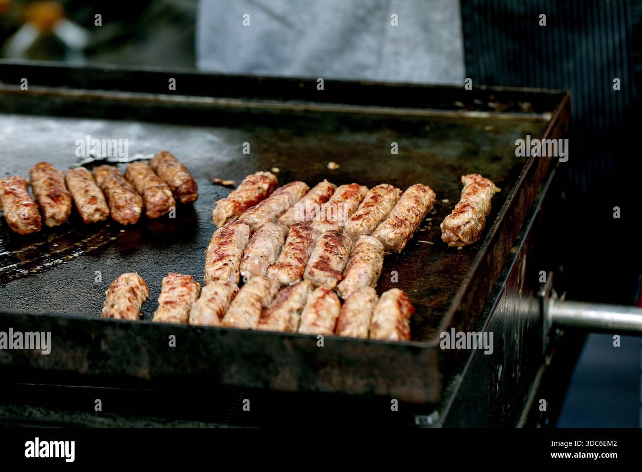 Kebab di carne tradizionali grigliati su piastra in metallo caldo. Succosi involtini di carne macinata a forma di salsiccia cucinati al mercato Street food. Cevapcici preparati balcanici Foto Stock