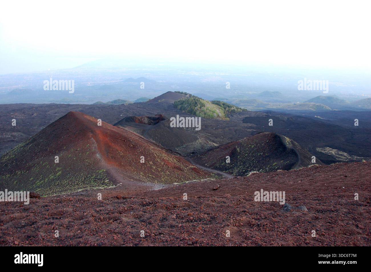 Cratere vulcanico sull'Etna in Sicilia con pendici lavici scure, terreno accidentato e una strada visibile lungo il bordo sullo sfondo Foto Stock