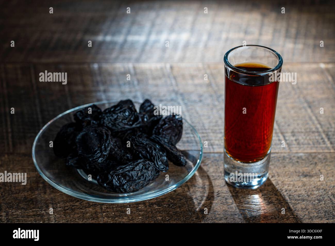 Brandy di prugne damson scure fatto in casa in bicchieri su un tavolo di legno, primo piano. Bere con prugne secche Foto Stock