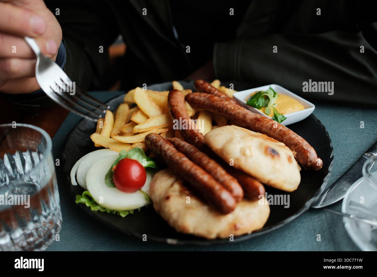 Salsicce alla griglia con patatine fritte, focaccia e salsa servite in un caffè. L'immagine mostra il concetto di cucina informale e comfort balcanico. Foto Stock