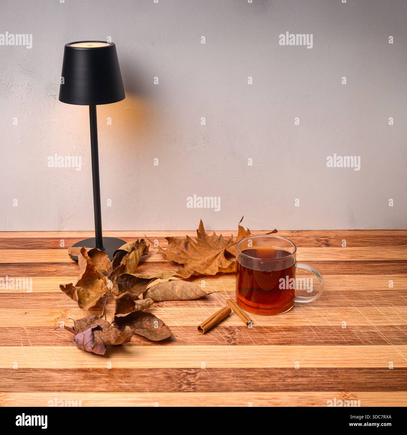 Le foglie autunnali su un tavolo rustico con tè caldo nelle vicinanze si trova Una piccola lampada. Foto Stock