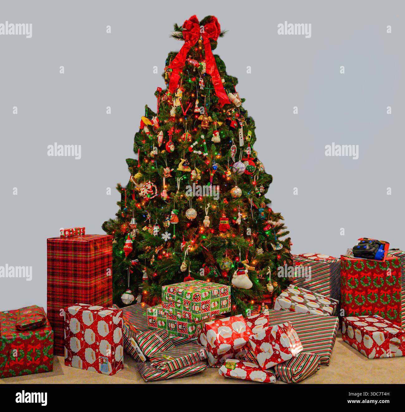 Albero di Natale decorato con diversi regali avvolti contro una parete grigia Foto Stock