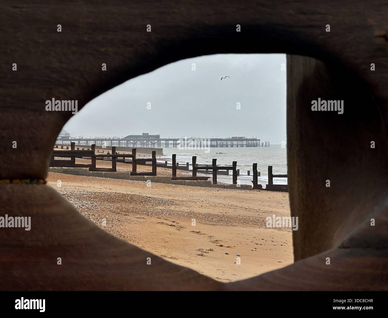 La spiaggia di Hastings, incorniciata da legni intemprati, con groynes che si estendono verso il mare e il molo che si staglia in lontananza Foto Stock