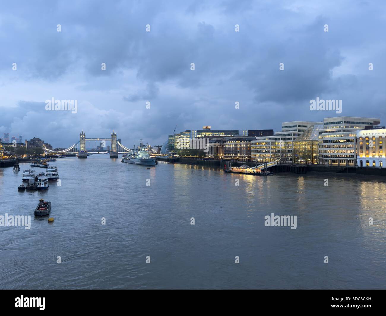Il Tower Bridge si illumina sul Tamigi al tramonto, con le luci della città che si riflettono sull'acqua. Foto Stock