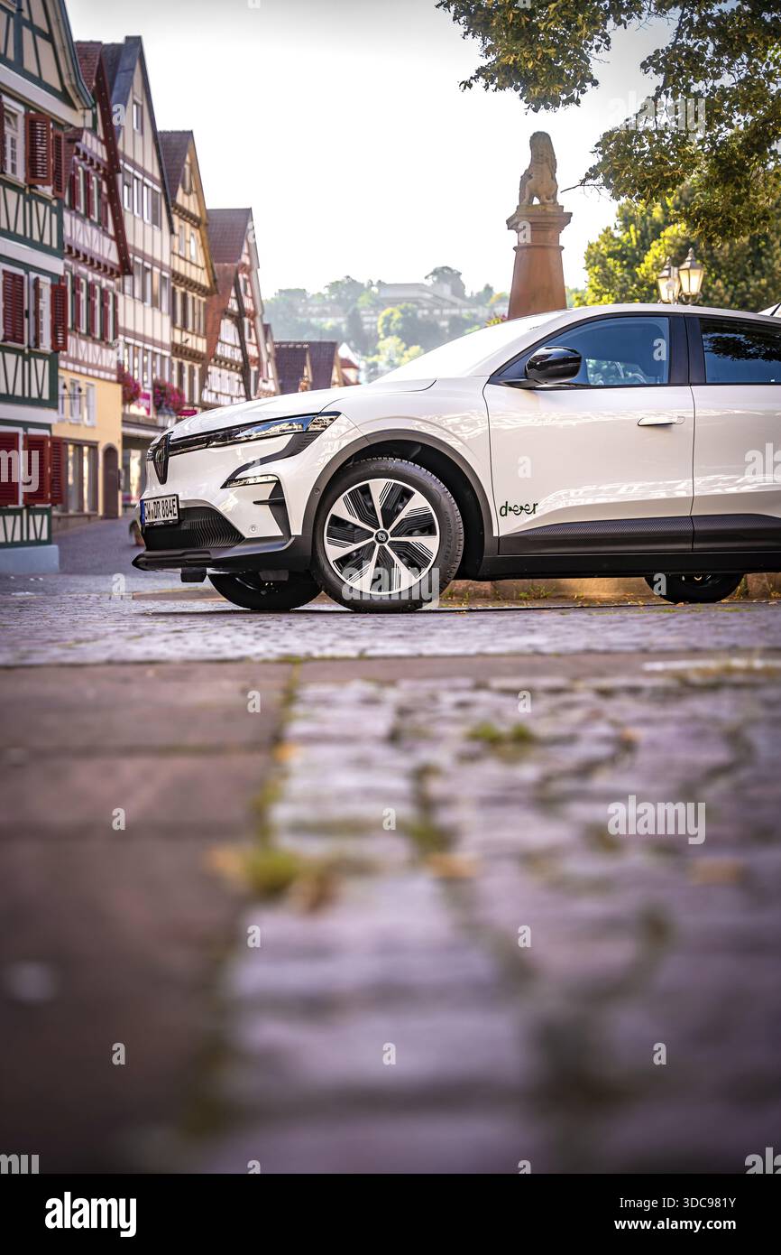 Auto bianca su strada acciottolata circondata da case e alberi a graticcio, Deer e-Carsharing, Renault Megane, Calw, Germania Foto Stock
