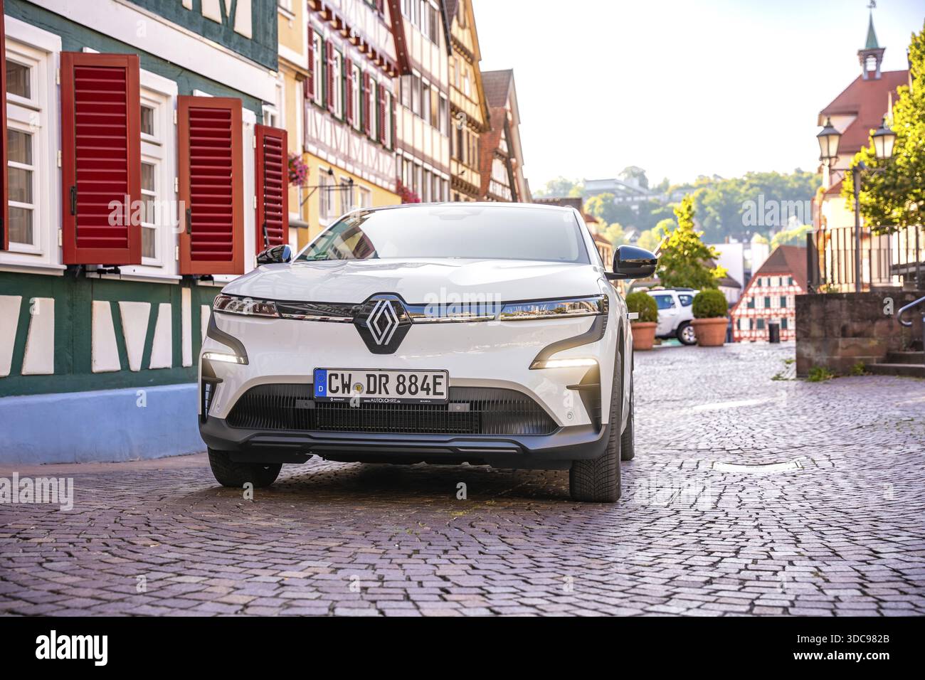 Auto bianca su strada acciottolata di fronte alle tradizionali case in legno al sole, Deer e-Carsharing, Renault Megane, Calw, Germania Foto Stock