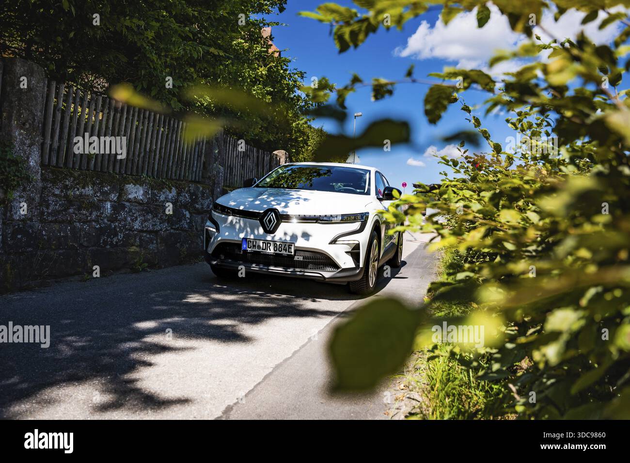 Auto bianca ombreggiata da foglie su una strada soleggiata, Deer e-Carsharing, Renault Megane, Calw, Germania Foto Stock