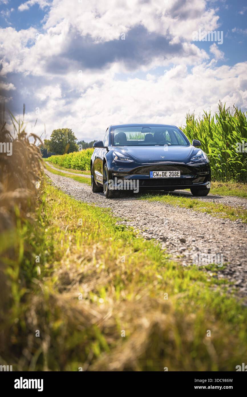 Auto nera su una strada stretta con campi e nuvole circostanti, Deer e-Carsharing, Tesla Model 3, Calw, Germania Foto Stock