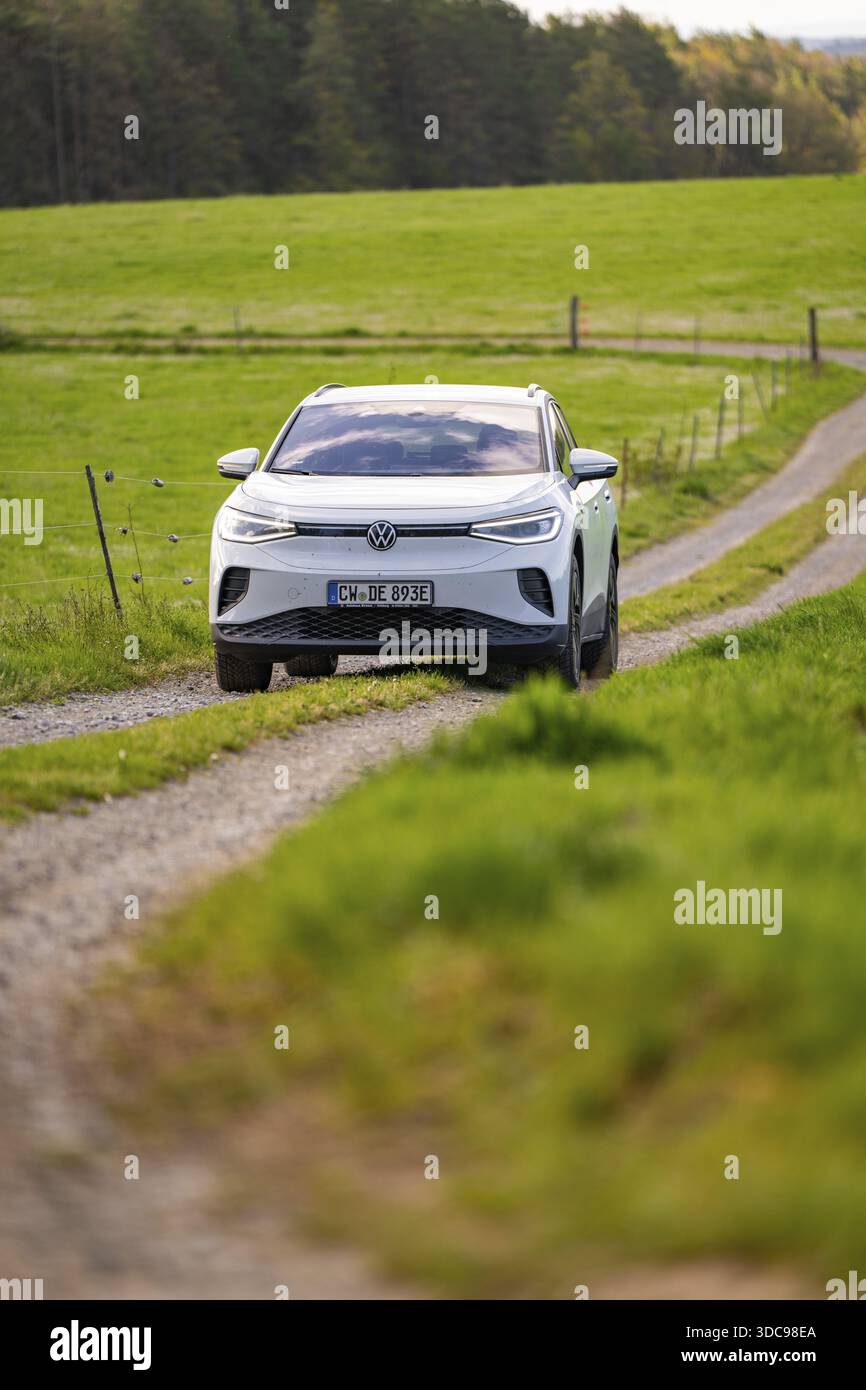 Auto bianca che guida su una strada sterrata attraverso prati verdi alla luce del giorno, Deer e-Carsharing, VW ID4, Calw, Germania Foto Stock