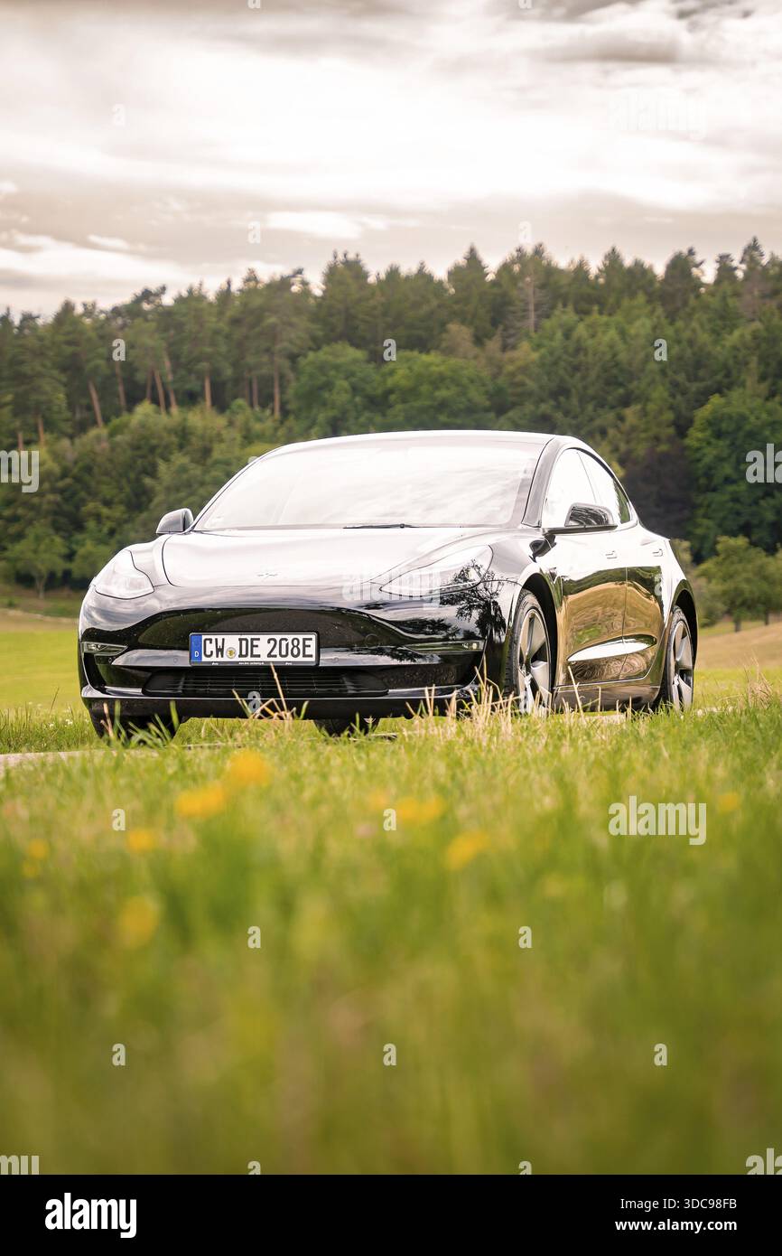 Auto nera su una strada di campagna con vista su campi verdi e boschi, Deer e-Carsharing, Tesla Model 3, Calw, Germania Foto Stock