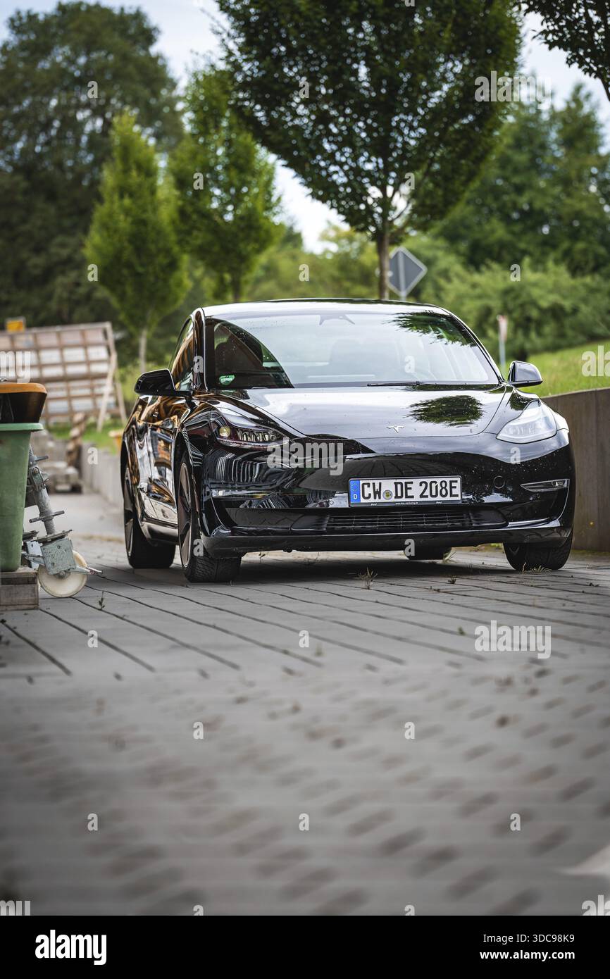 Auto nera dalla parte anteriore su una strada asfaltata con paesaggio di fondo, Deer e-Carsharing, Tesla Model 3, Calw, Germania Foto Stock