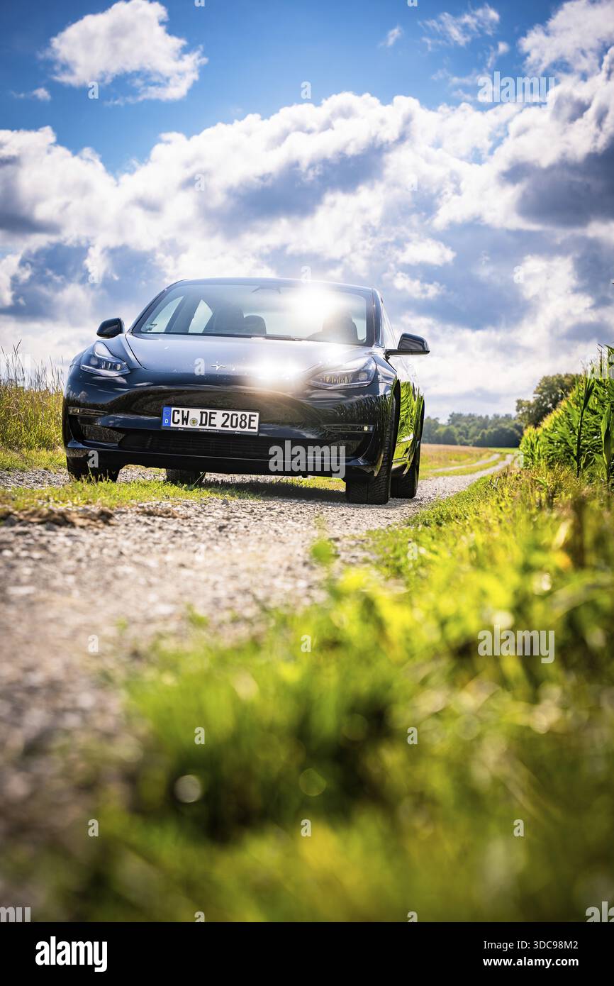 Auto nera che guida su una strada sterrata attraverso un paesaggio pittoresco sotto il cielo blu, Deer e-Carsharing, Tesla Model 3, Calw, Germania Foto Stock