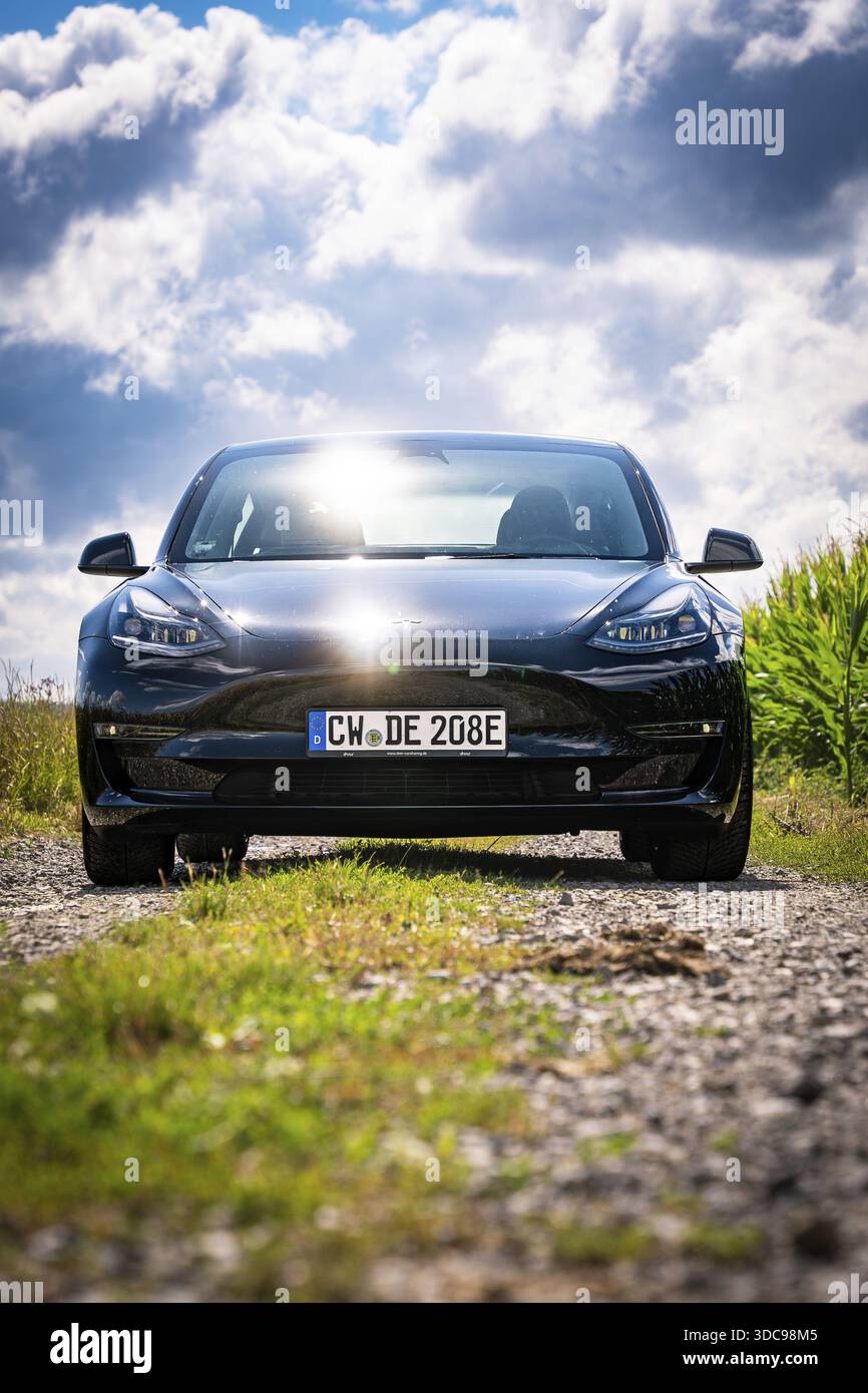Auto nera su strada rurale con il sole, circondata da campi e nuvole, Deer e-Carsharing, Tesla Model 3, Calw, Germania Foto Stock