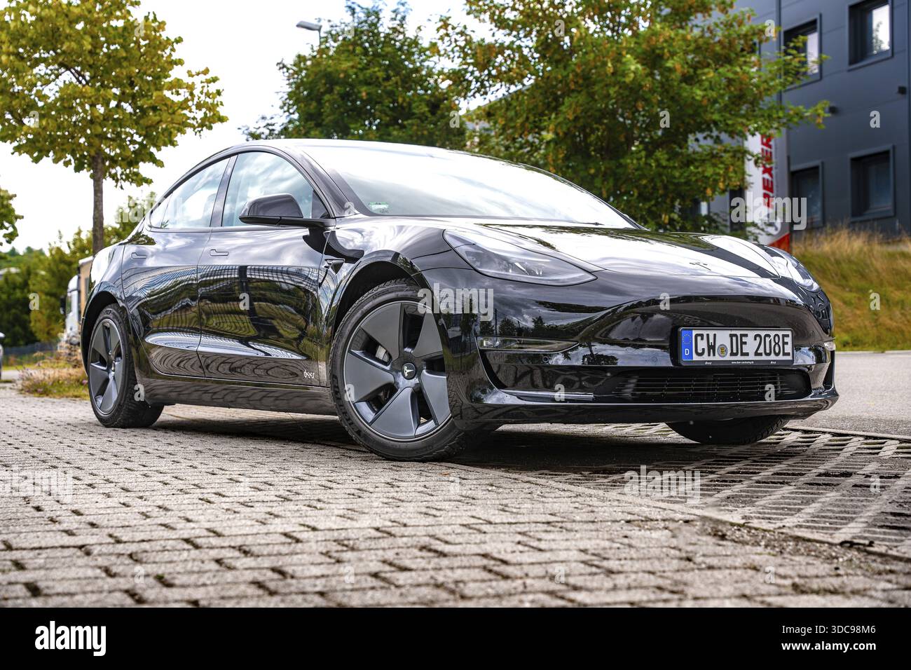 Auto nera su una strada urbana di fronte a edifici e alberi moderni, Deer e-Carsharing, Tesla Model 3, Calw, Germania Foto Stock