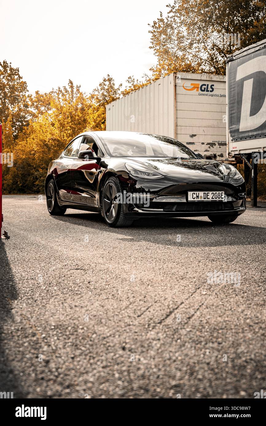 Auto nera su strada in un paesaggio autunnale soleggiato, Deer e-Carsharing, Tesla Model 3, Calw, Germania Foto Stock