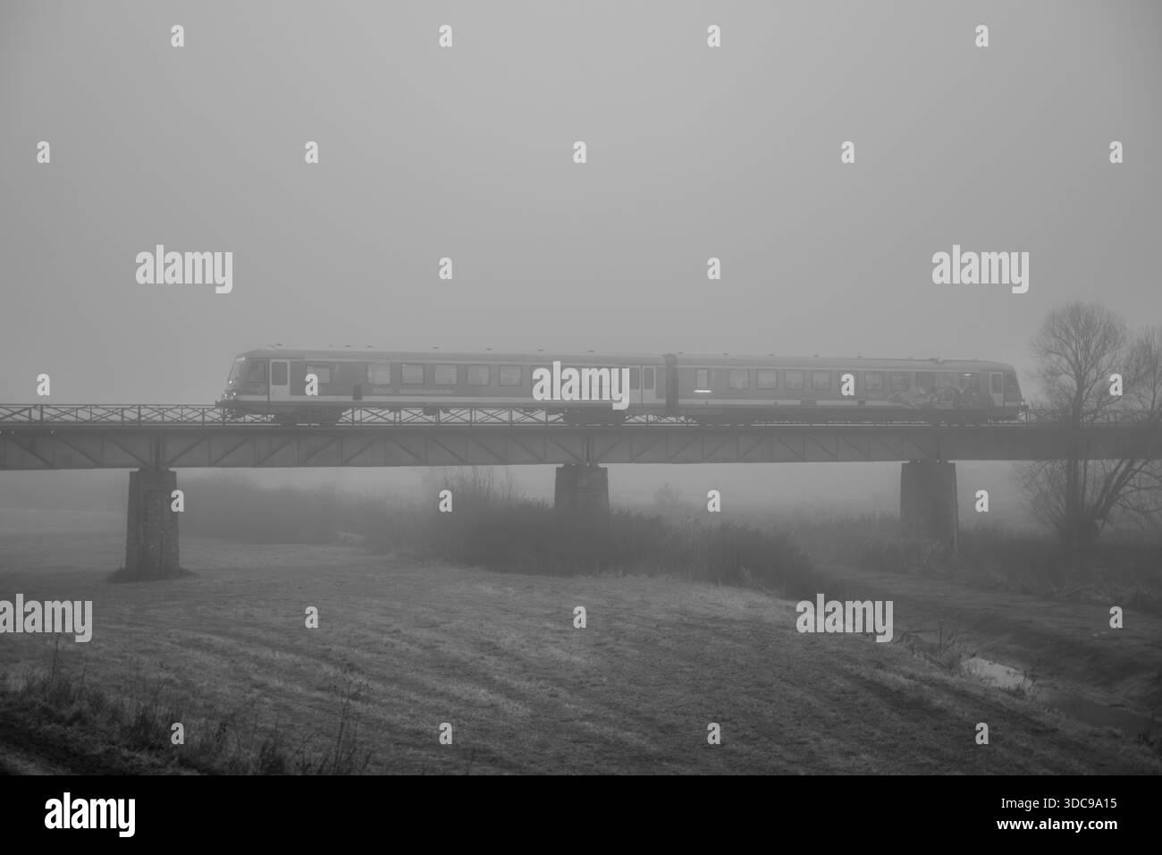 Un treno sta viaggiando su un ponte ferroviario. La nebbia avvolge il paesaggio. Si può vedere solo il profilo del treno. Sembra che la giornata sia grigia. B Foto Stock
