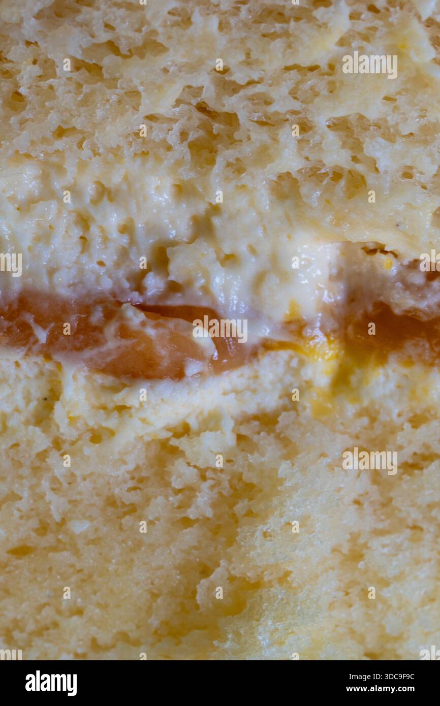 Una macro shot rivela gli strati distinti di una morbida torta di spugna giallastro, una cremosa glassa bianca e una vivace marmellata di frutta d'arancia. Foto Stock