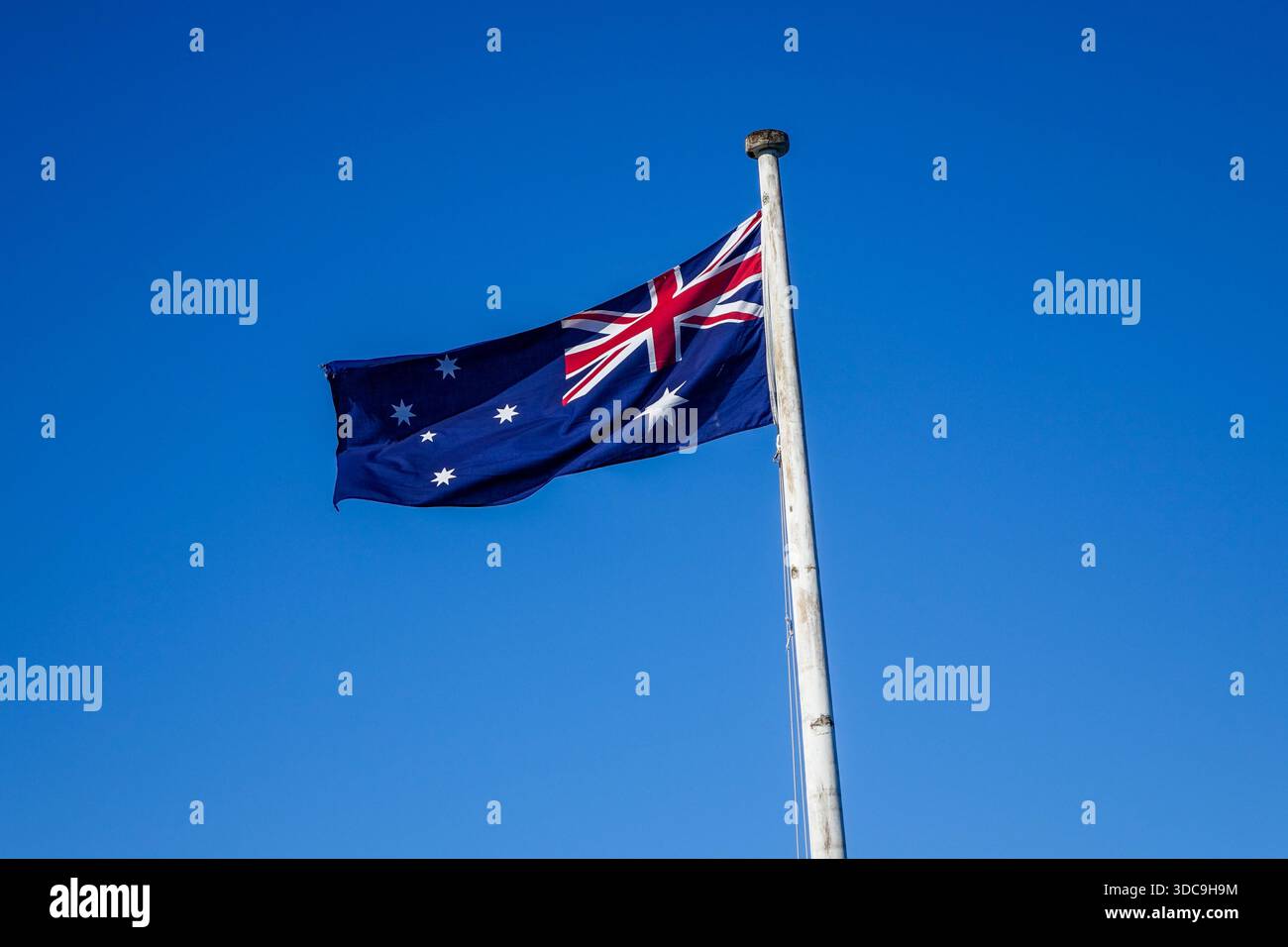 La bandiera blu australiana sventola vigorosamente da un'asta bianca, contrastando con un cielo azzurro chiaro e luminoso in una giornata di sole. Foto Stock