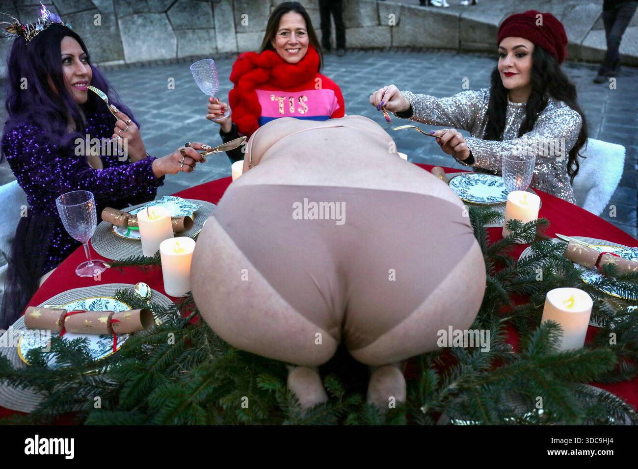 Londra, Regno Unito. 20 dicembre 2025. I commensali sollevano coltelli e forchette come se iniziassero a intagliare l'offerta umana invece di un solito tacchino durante l'installazione. Il movimento artistico globale vegano "SpeciesismWTF" ha creato un'installazione artistica sulla South Bank di Londra. L'opera d'arte, intitolata "il pollame non è umano(e)", colloca un essere umano nella posizione di un animale al tavolo della cena di Natale. Essi affermano che, a livello globale, miliardi di uccelli vengono confinati, mutilati e macellati ogni anno per uova e carne. Credito: SOPA Images Limited/Alamy Live News Foto Stock