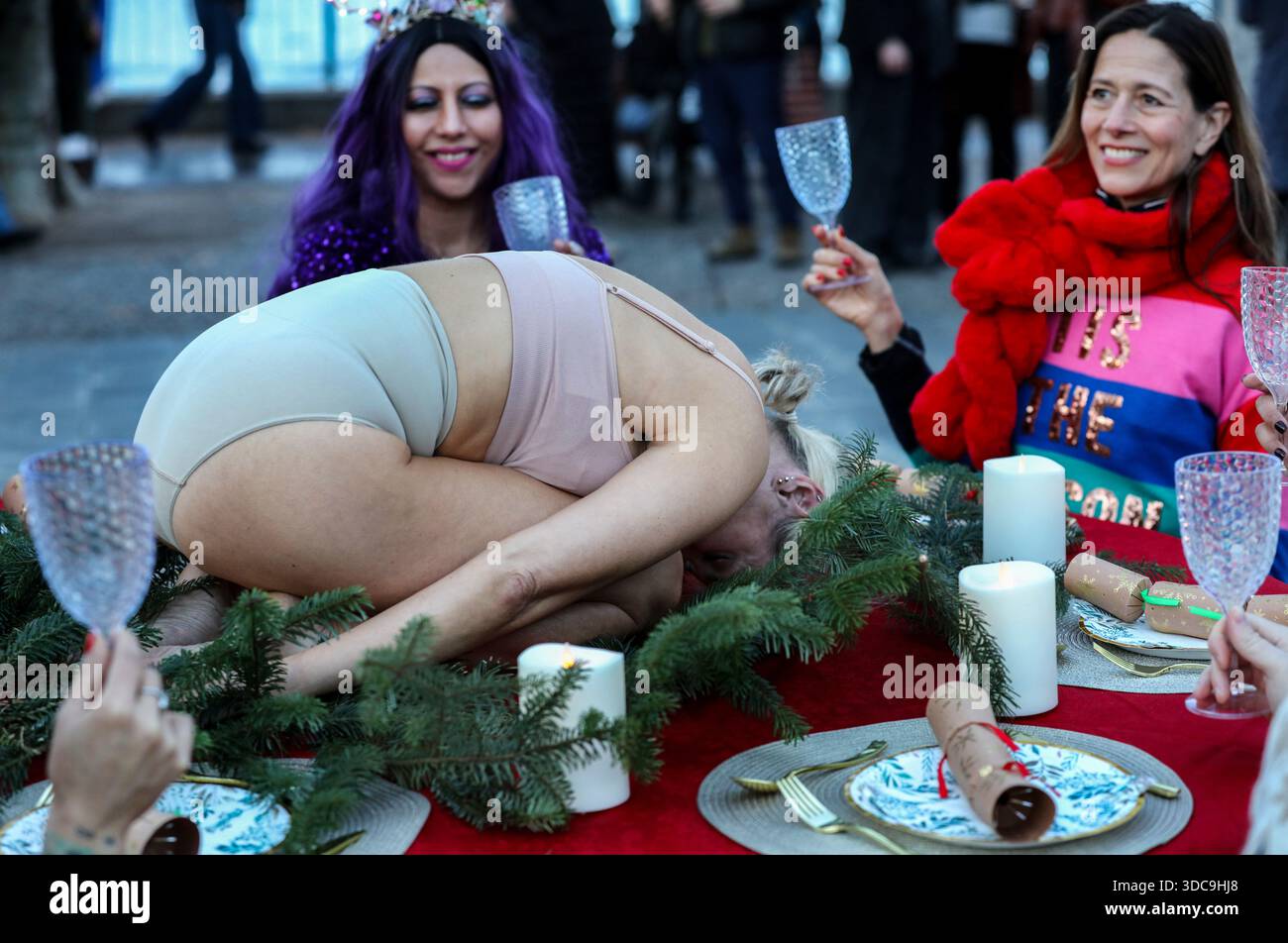Londra, Regno Unito. 20 dicembre 2025. I commensali alzano i loro bicchieri come un essere umano viene presentato sul tavolo invece che sul pollame durante l'installazione. Il movimento artistico globale vegano "SpeciesismWTF" ha creato un'installazione artistica sulla South Bank di Londra. L'opera d'arte, intitolata "il pollame non è umano(e)", colloca un essere umano nella posizione di un animale al tavolo della cena di Natale. Essi affermano che, a livello globale, miliardi di uccelli vengono confinati, mutilati e macellati ogni anno per uova e carne. Credito: SOPA Images Limited/Alamy Live News Foto Stock