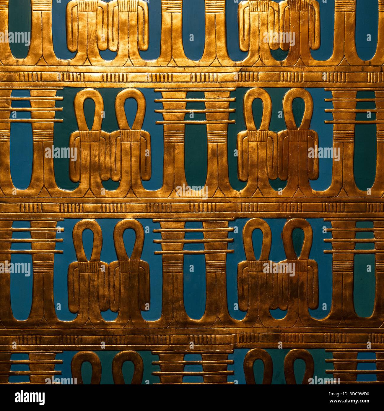 Vista dettagliata di un rilievo geroglifico dorato in stile egiziano antico con figure simboliche ripetute su uno sfondo blu profondo, ispirato alla a faraonica Foto Stock