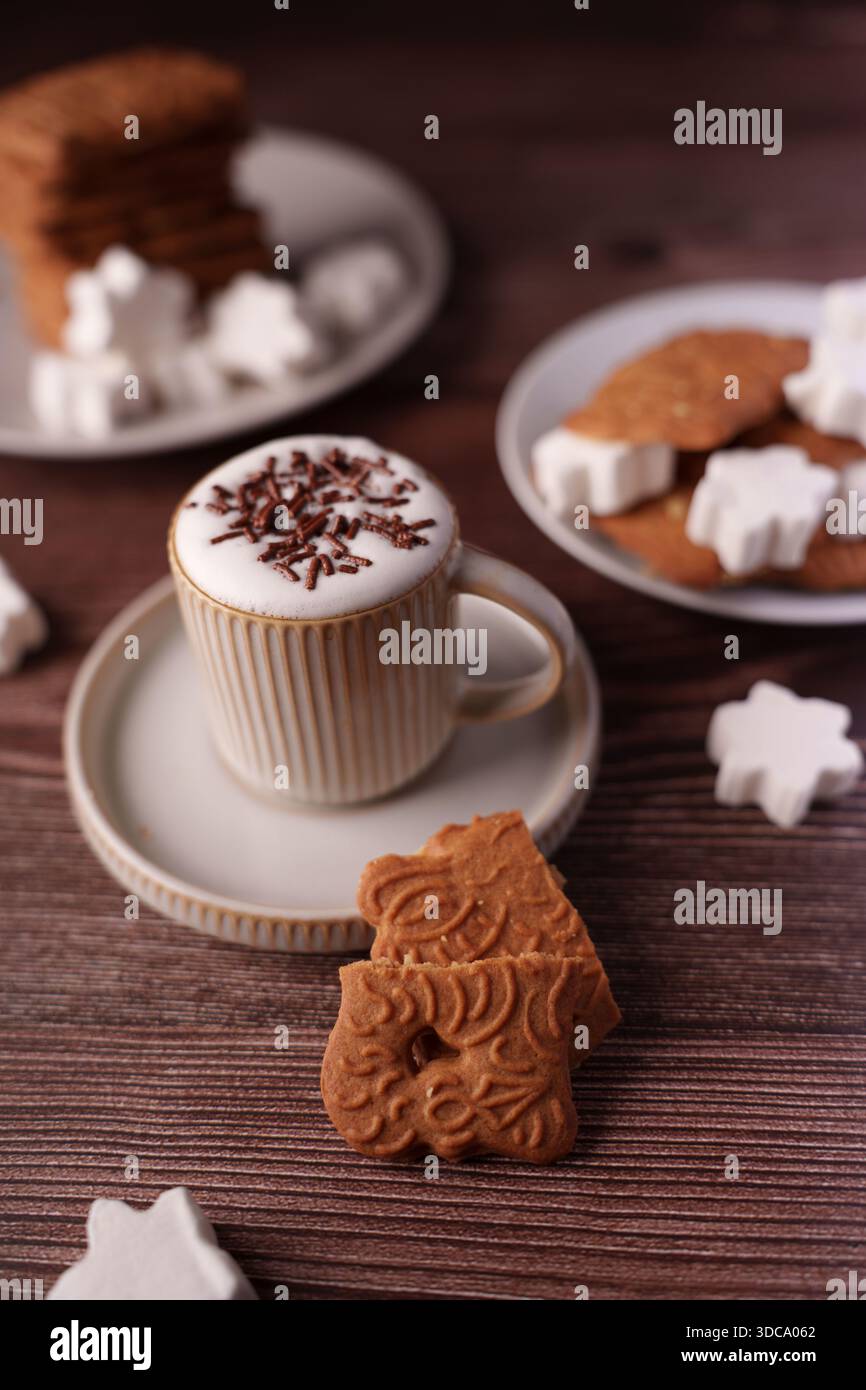 ambiente accogliente con cappuccino e biscotti sul tavolo di legno, con latte art con spruzzette di cioccolato e biscotti decorativi completati da bianco Foto Stock