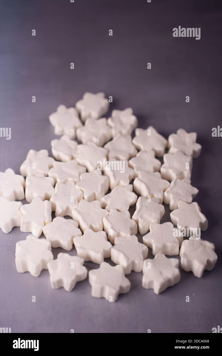 disposizione di confetti bianchi a forma di stella su una superficie grigia liscia che evoca un'estetica calma e minimalista con luci soffuse e ombre delicate, dicembre Foto Stock