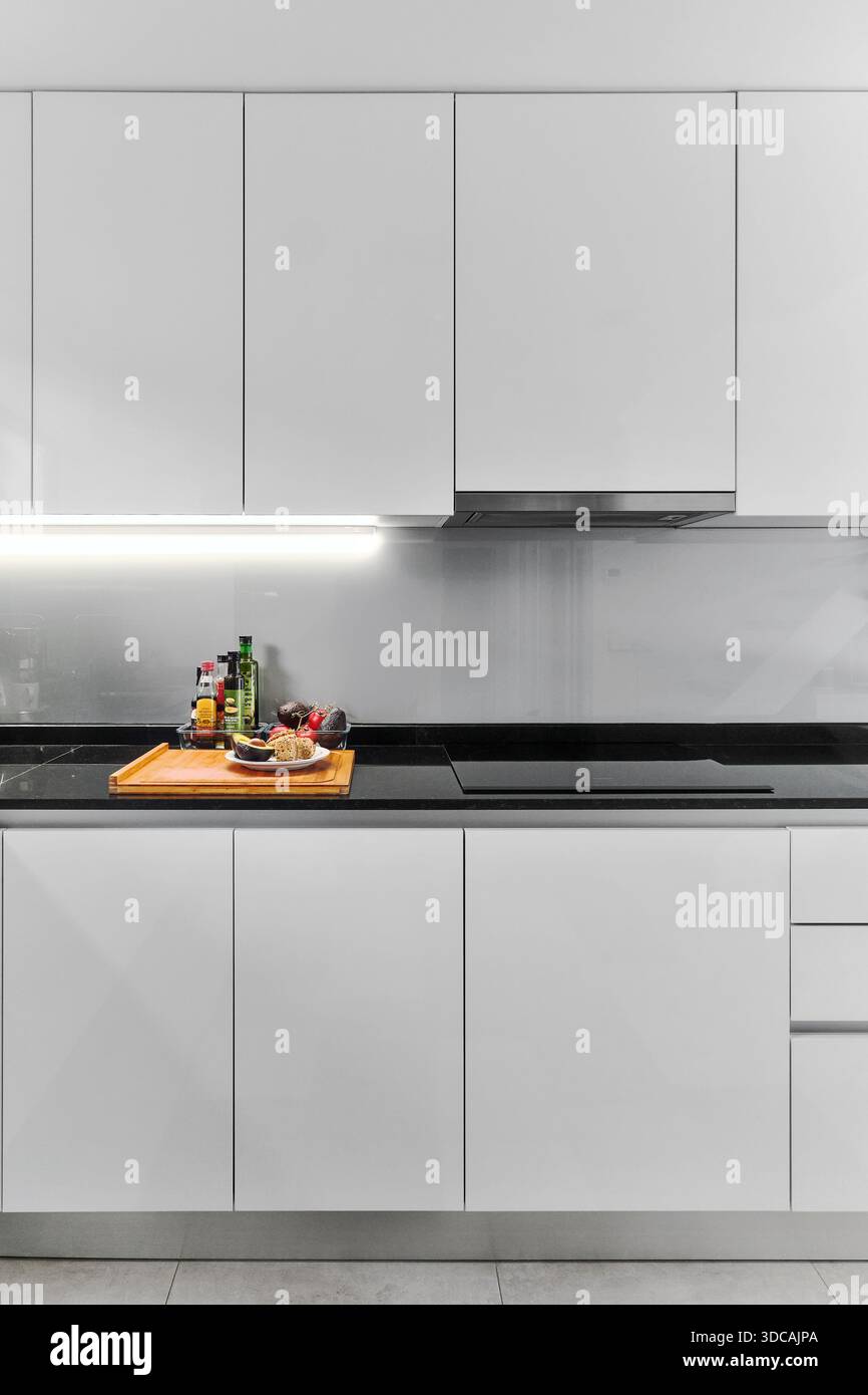 Cucina moderna con armadi bianchi lucidi, ripiani in marmo nero e illuminazione a LED sotto l'armadio Foto Stock