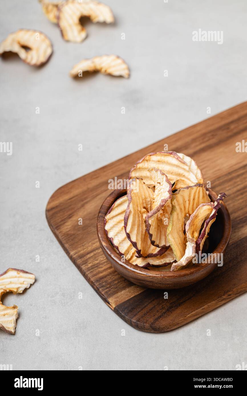 Le patatine di mele in una ciotola di legno su sfondo grigio chiaro. Uno spuntino sano e delizioso pieno di vitamine. Adatto per vegetariani. Foto Stock