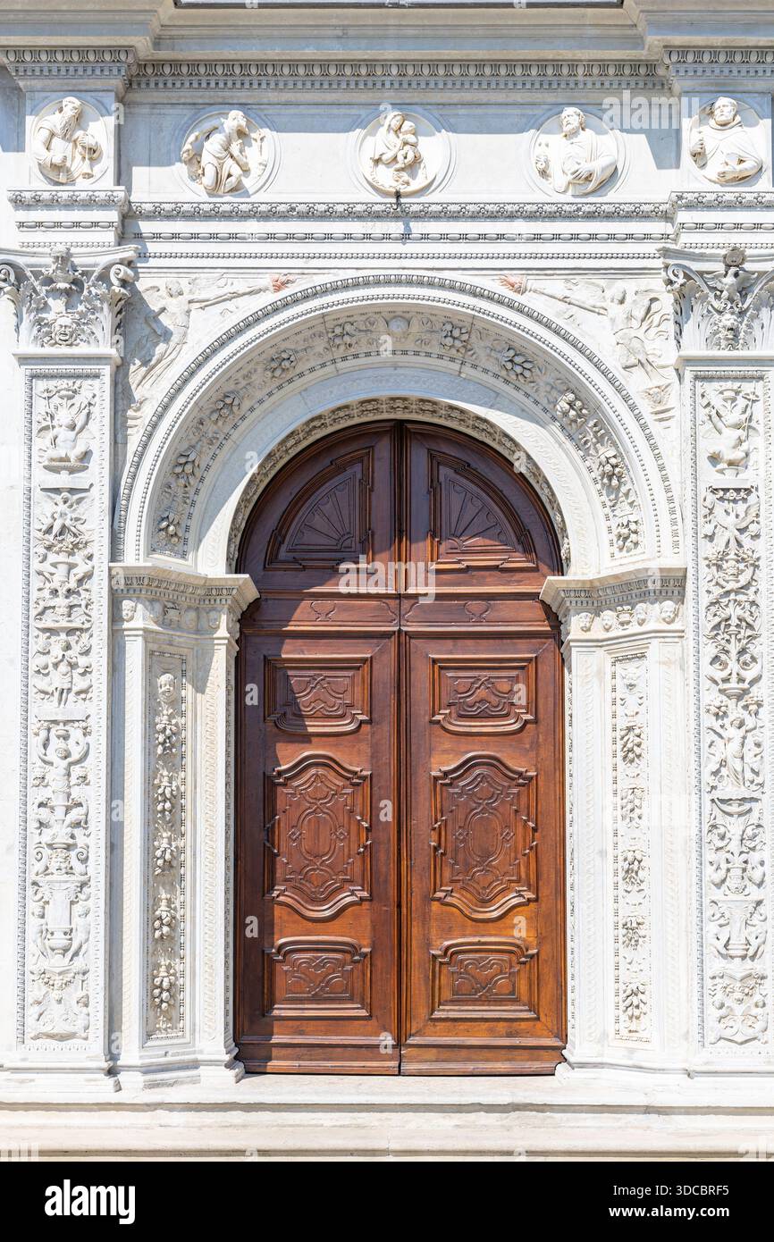 Una grandiosa entrata storica caratterizzata da un arco in pietra riccamente intagliato, rilievi decorativi e una doppia porta in legno scuro. Perfetto per architettura, tradizione, Foto Stock