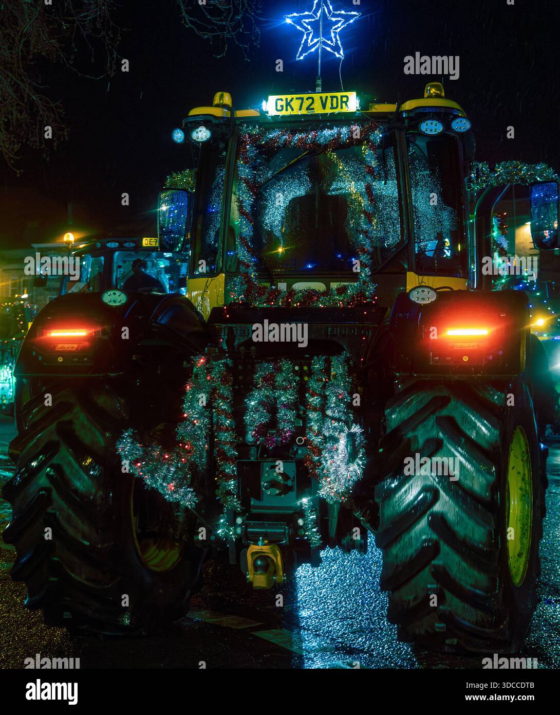 Vista posteriore di un trattore decorato con luci e tinsel che partecipano a una sfilata natalizia di notte sotto la pioggia Foto Stock