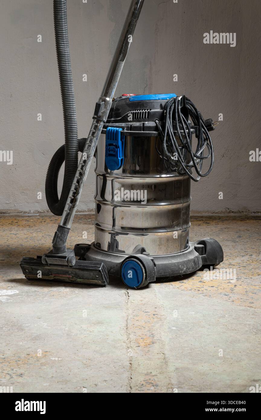 Un aspirapolvere in metallo lucido dal design blu e nero, posizionato su un pavimento in cemento con texture e usura visibili Foto Stock