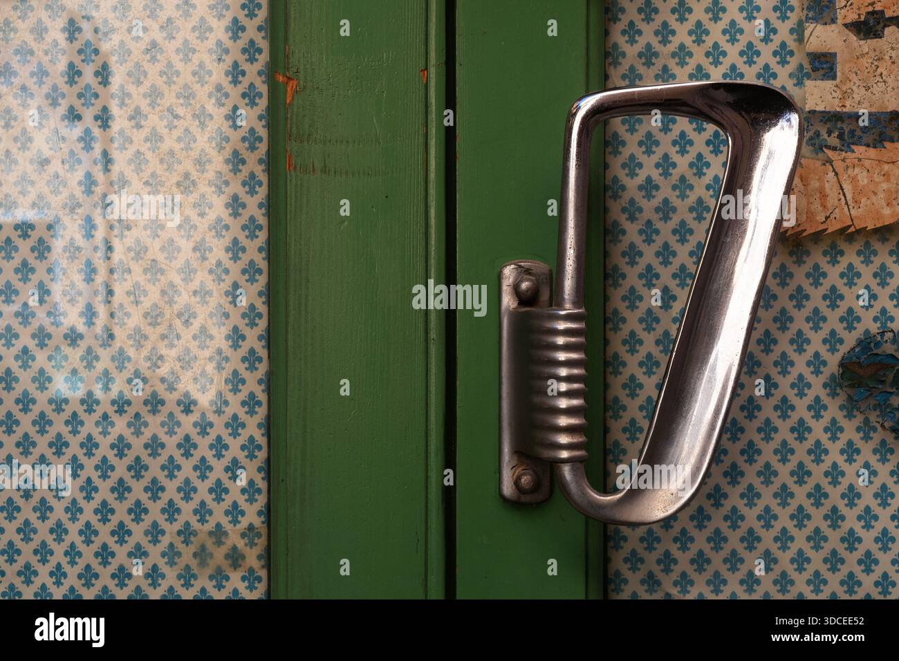 Maniglia in metallo vintage su porta in legno verde con carta da parati a motivi geometrici Foto Stock