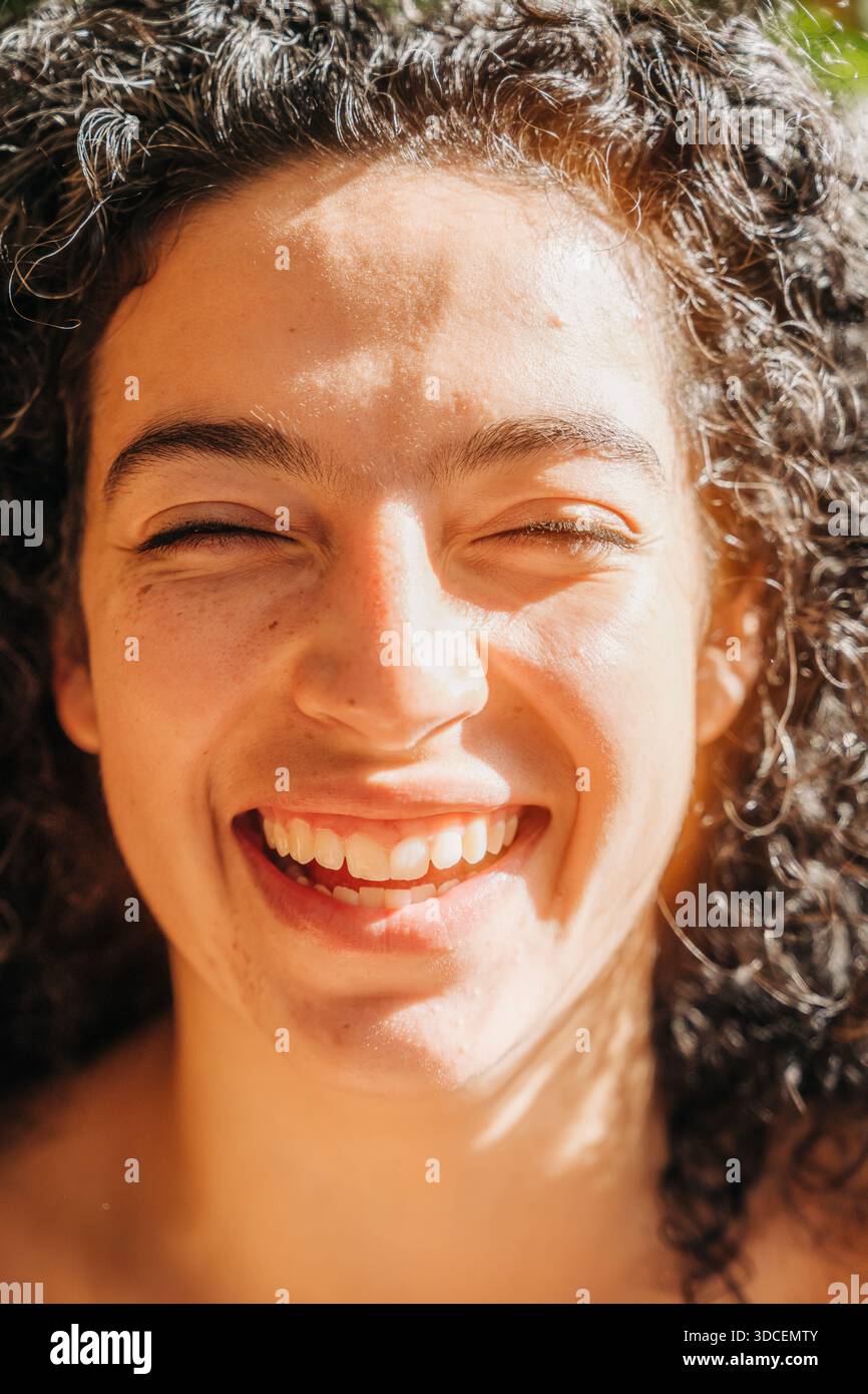 Primo piano di una donna che sorride brillantemente in una calda luce naturale del sole Foto Stock