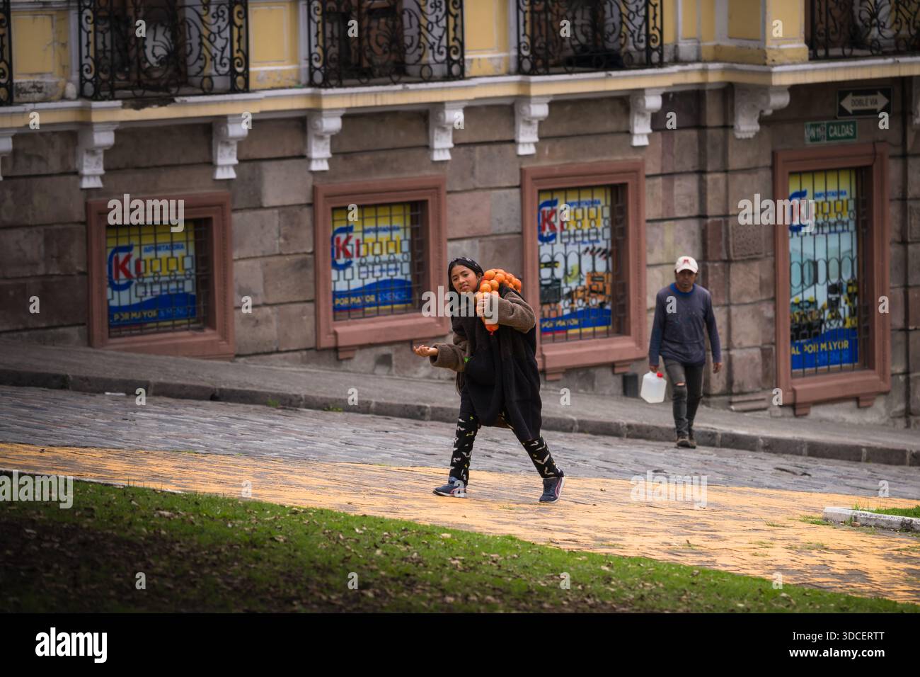 Quito, Ecuador - 17 ottobre 2025: La vista di una donna si muove con fiducia su un sentiero vicino a un edificio con finestre decorative. Foto Stock