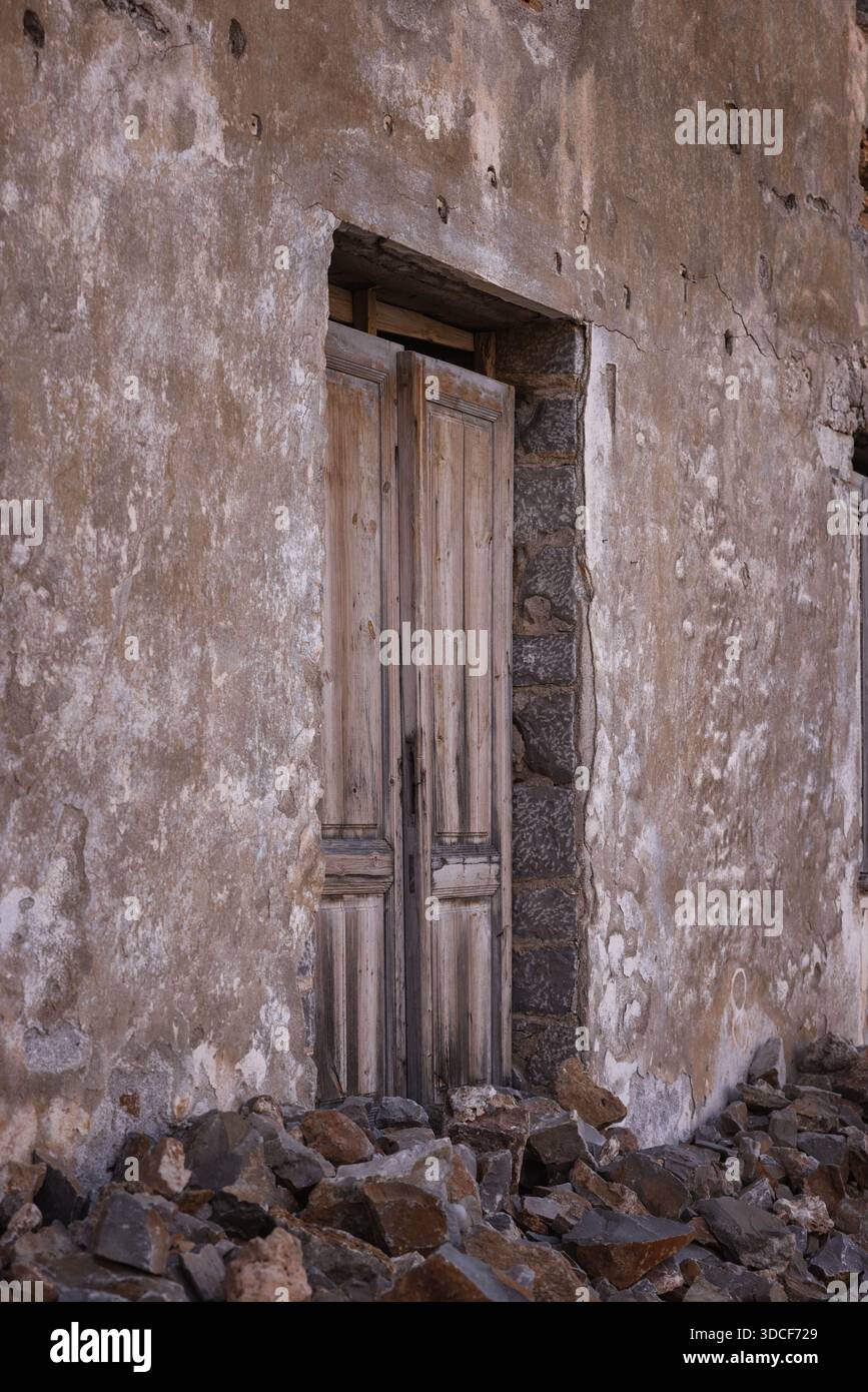 Porta di legno intemprata in un edificio in decadenza sull'isola fortezza di Spinalonga, con mura e macerie, Creta Grecia. Rovine storiche abbandonate. Foto Stock