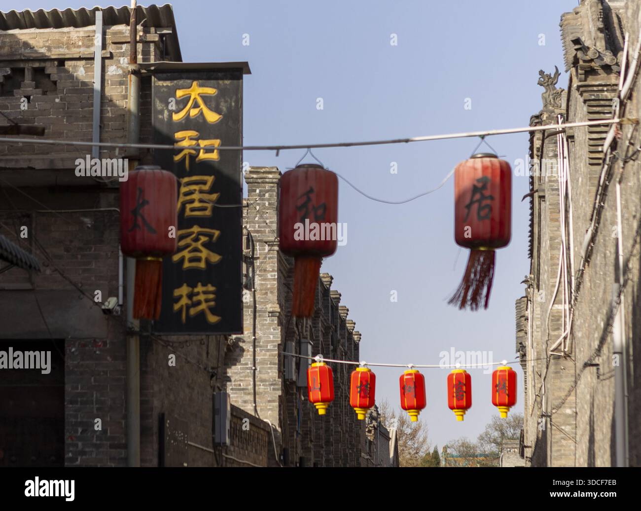 Veduta delle vivaci lanterne rosse avvolte attraverso una strada stretta, contrastando con gli edifici in mattoni antichi e il cielo azzurro, Pingyao, Shanxi, Cina. Foto Stock