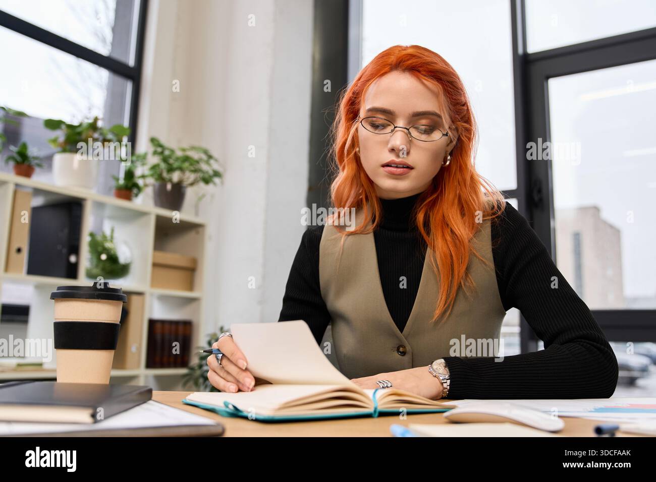 Una bella giovane donna sta scrivendo diligentemente appunti in uno spazio di lavoro elegante, circondato da piante. Foto Stock